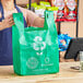 A woman holding a green Choice plastic t-shirt bag in front of a wooden counter.