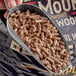A person holding a metal cup with a scoop of Bear Mountain maple wood pellets.