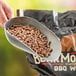 A person using a metal scoop to hold Bear Mountain Maple BBQ pellets.