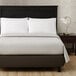 A Berkshire Hospitality twin size gray mist pucker jacquard top sheet on a bed with a black headboard.