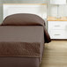A brown Berkshire Hospitality CozyCare Designs fitted coverlet on a bed with a pillow.