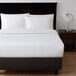 A bed with Berkshire Hospitality white top sheets and pillows on a nightstand with a lamp.