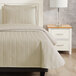 A twin size bed with a Berkshire Hospitality botanical leaf quilt throw in a room with a nightstand and lamp.