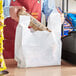 A person putting a carton of food into a white plastic t-shirt bag.