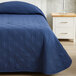 A navy blue Berkshire Hospitality CozyCare bedspread on a bed next to a white nightstand.