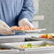 A person in a blue uniform holding a Vollrath stainless steel tray of food.