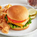 A cheeseburger with lettuce and tomato on a King's Hawaiian hamburger bun with potato chips on a plate.