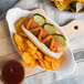 A hot dog in a Hauswald Sliced Hot Dog Bun with pickles and chips on a plate.