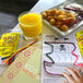 A table with a Wikki Stix Mini Play Pack, a plate of food, and a glass of orange juice.