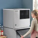 A woman standing next to a large Hoshizaki air cooled ice machine in a professional kitchen.