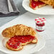 A croissant on a plate with Bonne Maman strawberry preserves.