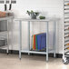 A galvanized steel undershelf on a metal work table with a rack of vegetables.