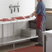 A man in a red apron and gloves cutting meat on a poly top work table with an adjustable stainless steel undershelf.