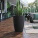 A Lancaster Table & Seating black planter with a potted plant on a wood deck.