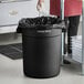 A woman holding a white towel over a black Advantage Supplies trash can.