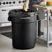 A black Advantage Supplies 44 gallon round commercial trash can with a black bag inside, a person putting a sponge in it.