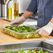 A person preparing broccoli in a Vollrath clear polycarbonate food pan.