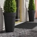 Two Lancaster Table & Seating black planters with plants in them.