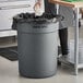 A woman standing next to a gray Advantage Supplies commercial trash can with a black bag inside.