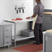 A man in a professional kitchen with Regency adjustable stainless steel undershelves on a work table.