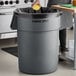 A woman standing next to a gray Advantage Supplies commercial trash can.