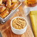 A bowl of Sir Kensington's spicy brown mustard on a table with food.