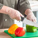 A person in a white coat cutting a green bell pepper with Choice disposable poly gloves.