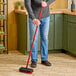 A man using a Libman red floor scrub to clean the floor.