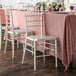 Lancaster Table & Seating champagne resin Chiavari chairs on a table with a pink tablecloth.