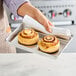 A person holding a Baker's Lane aluminum sheet pan with cinnamon rolls.