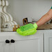 A person wearing a green Libman microfiber duster mitt cleaning a white cabinet.