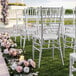 A group of Lancaster Table & Seating steel reinforced silver resin Chiavari chairs on the grass with flowers.