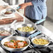 A woman cooking meat in a Vigor aluminum fry pan on a stove.