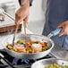 A person cooking food in a Vigor aluminum fry pan with tongs.