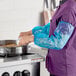 A person wearing blue polyethylene food-safe sleeves while cooking at a stove.
