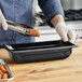 A person in gloves using a Vollrath black polycarbonate food pan to serve food.