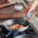 A person cooking shrimp in a Vigor A3000 series aluminum fry pan with a black non-stick surface and a blue silicone grip.