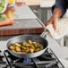 A hand cooking vegetables in a Vigor A3000 Series aluminum fry pan on a stove.