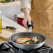 A person cooking salmon and vegetables in a Vigor A3000 Series aluminum fry pan with non-stick coating.