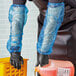 A person wearing black gloves and Lavex blue plastic sleeves holding a plastic container.