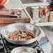 A person using a Vigor A3000 fry pan to cook meat on a stove.