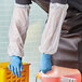 A person in blue gloves pouring liquid into a plastic container.