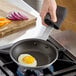 A hand holding a Vigor A3000 Series aluminum fry pan with a fried egg in it.