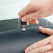 A hand uses a Lavex stainless steel paper towel dispenser key to open a toilet paper dispenser.