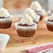 A group of 2 1/4" x 1 7/8" white fluted jumbo cupcakes with white frosting on a cooling rack.