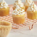 A Baker's Lane kraft fluted mini baking cup with a cupcake with white frosting and gold beads.