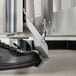 A metal left foot pedal kit attached to the bottom of a stainless steel appliance, shown being pressed by a black shoe.