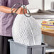 A woman holding a white Glad ForceFlex trash bag full of garbage in a kitchen.