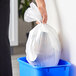 A hand holding a Glad small white trash bag with Febreze scent in a blue trash can.