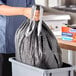 A person holding a Hefty Ultra Strong Black Drawstring trash bag over a trash can.